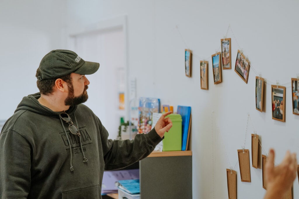 A bearded man wearing a dark olive green hoodie and a matching baseball cap.