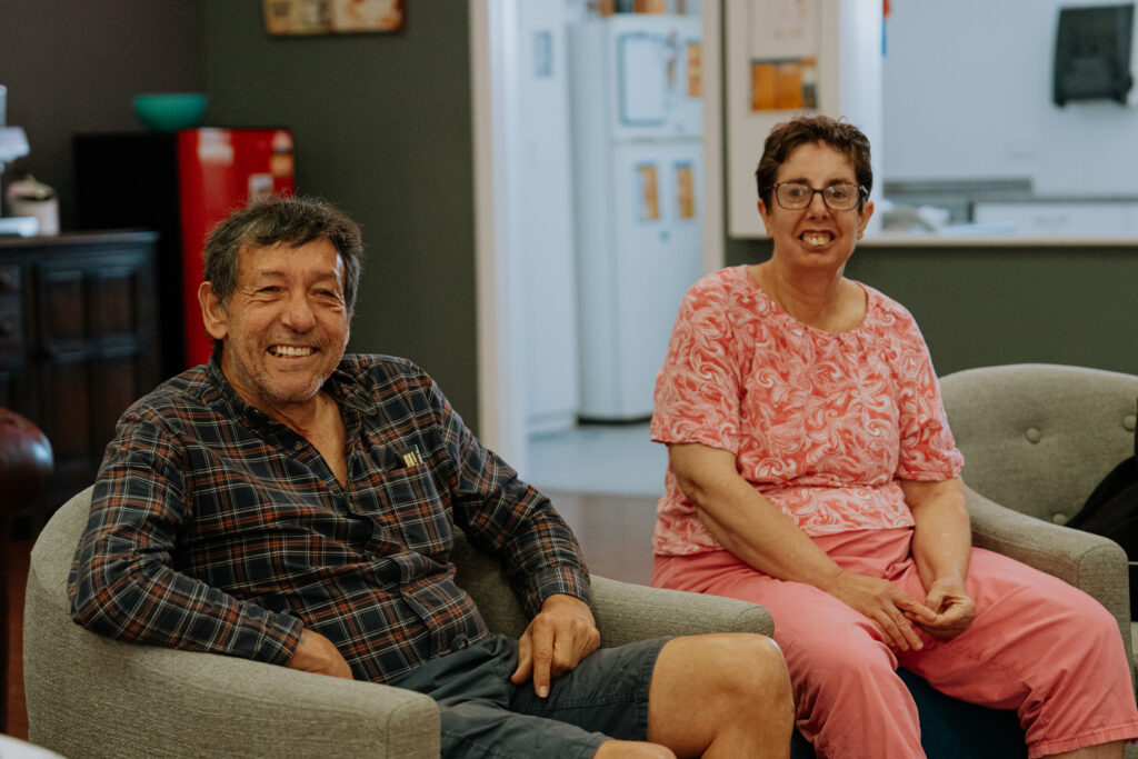 Two people sitting in matching grey armchairs in what looks like a living or communal room.