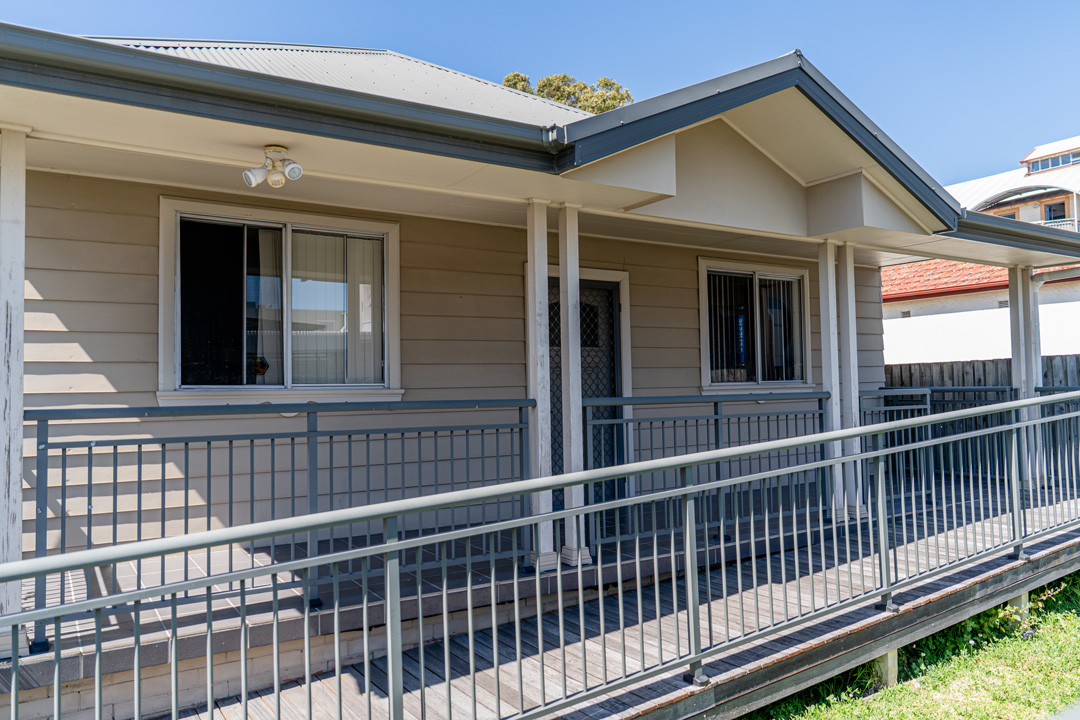 A beige, single-storey house with a grey roof and a long accessible ramp leading up to the front door.