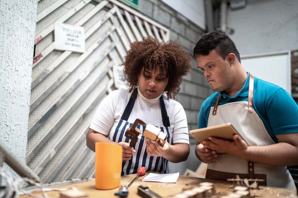 A woman and a young man with Down syndrome, collaborating in a workshop or studio.