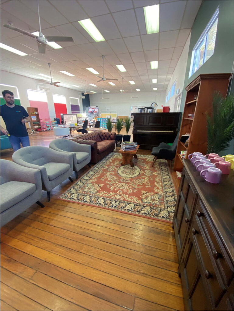 A large, brightly lit room with polished wooden floors, used as a casual communal or lounge area.